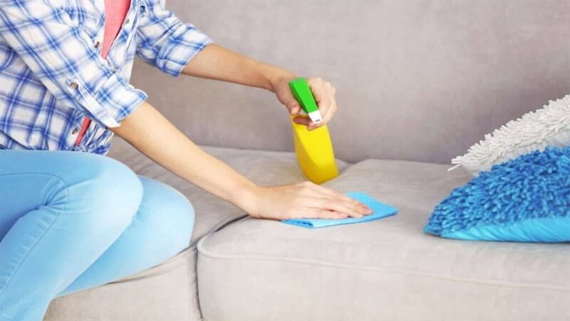 تمیز کردن مبل پارچه ای با استفاده از محلول مخصوص توسط یک فرد در منزل